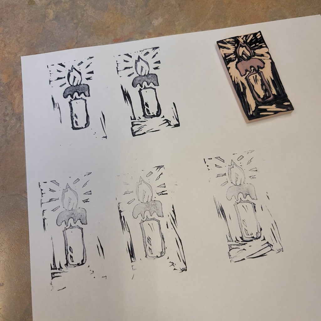 Prints of hand-carved candle stamps on white paper, with one stamp still on the block.